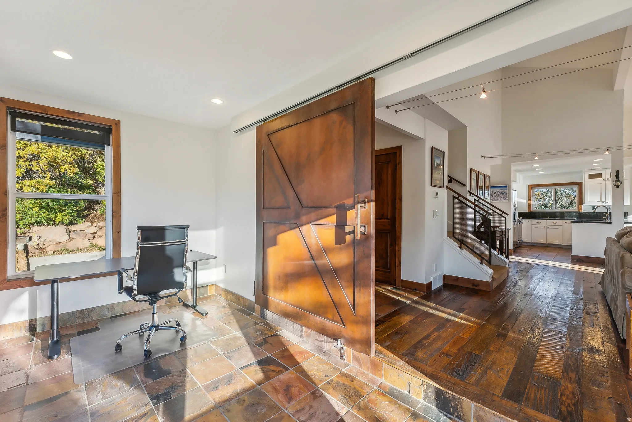 Spacious room featuring multi-toned stone tile flooring, a large window with natural wood trim, and recessed lighting