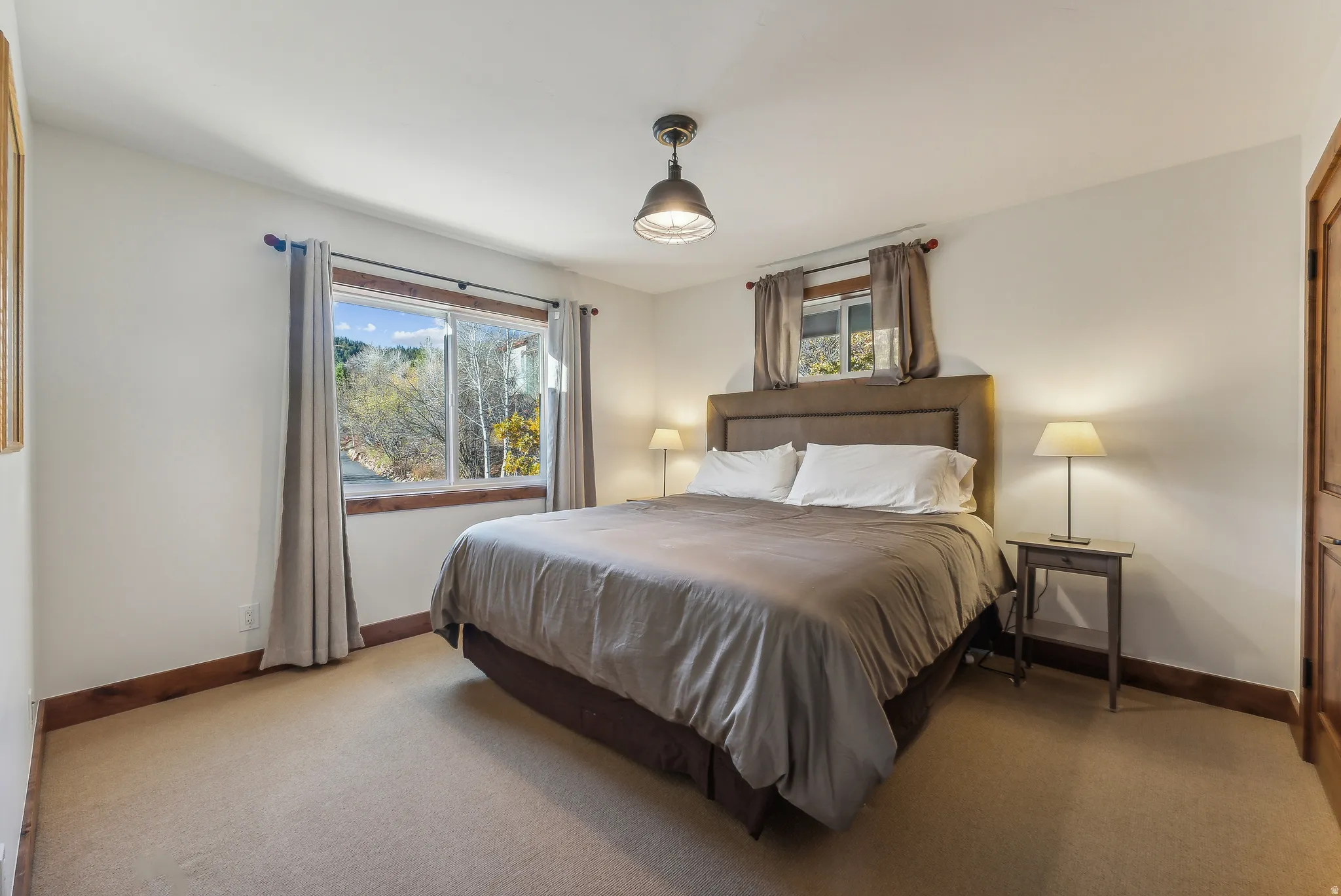 Carpeted bedroom with white walls, wood trim, and a window framing outdoor scenery