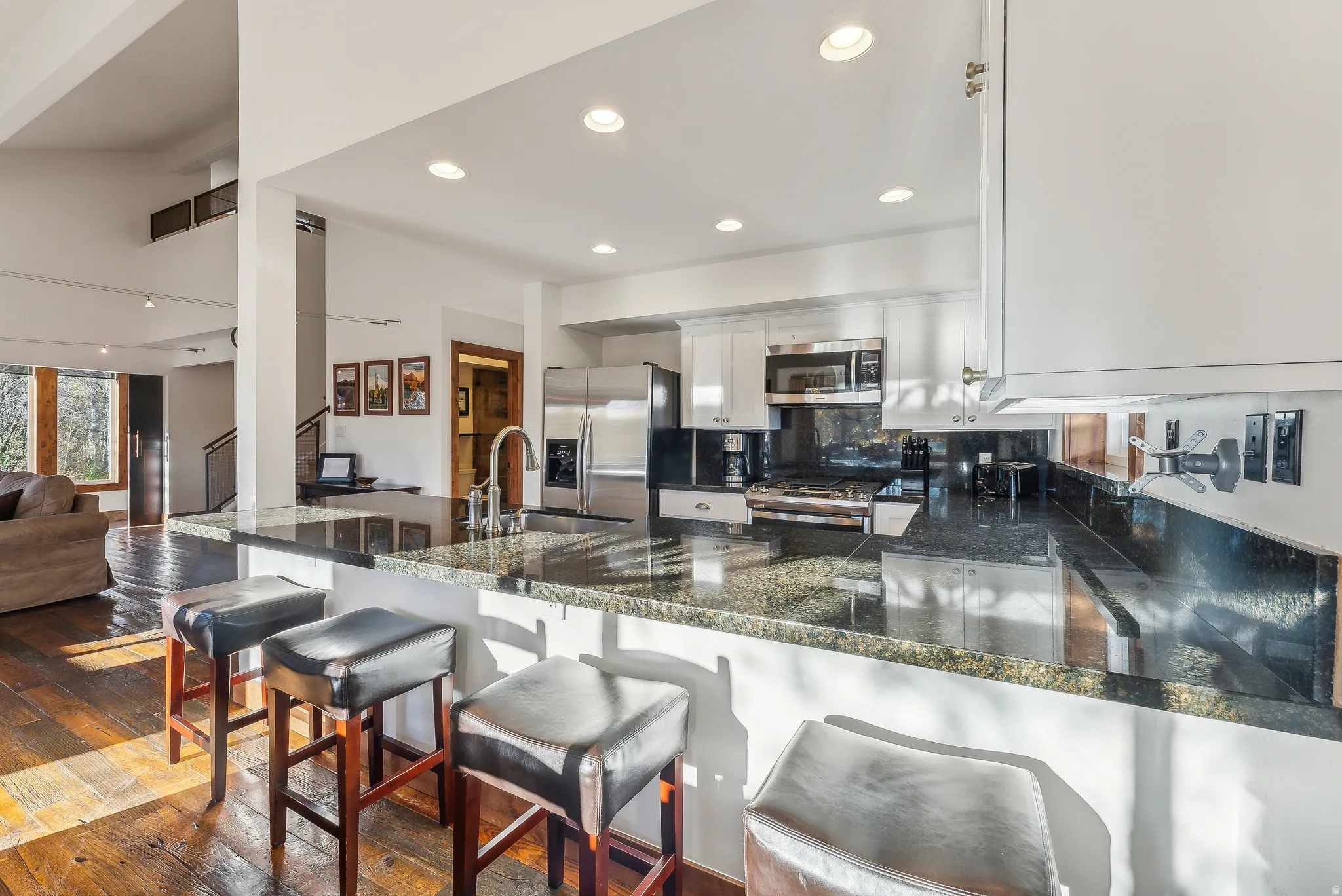 Kitchen featuring a granite breakfast bar, stainless steel appliances, white cabinetry, recessed lighting, and a dark tile backsplash
