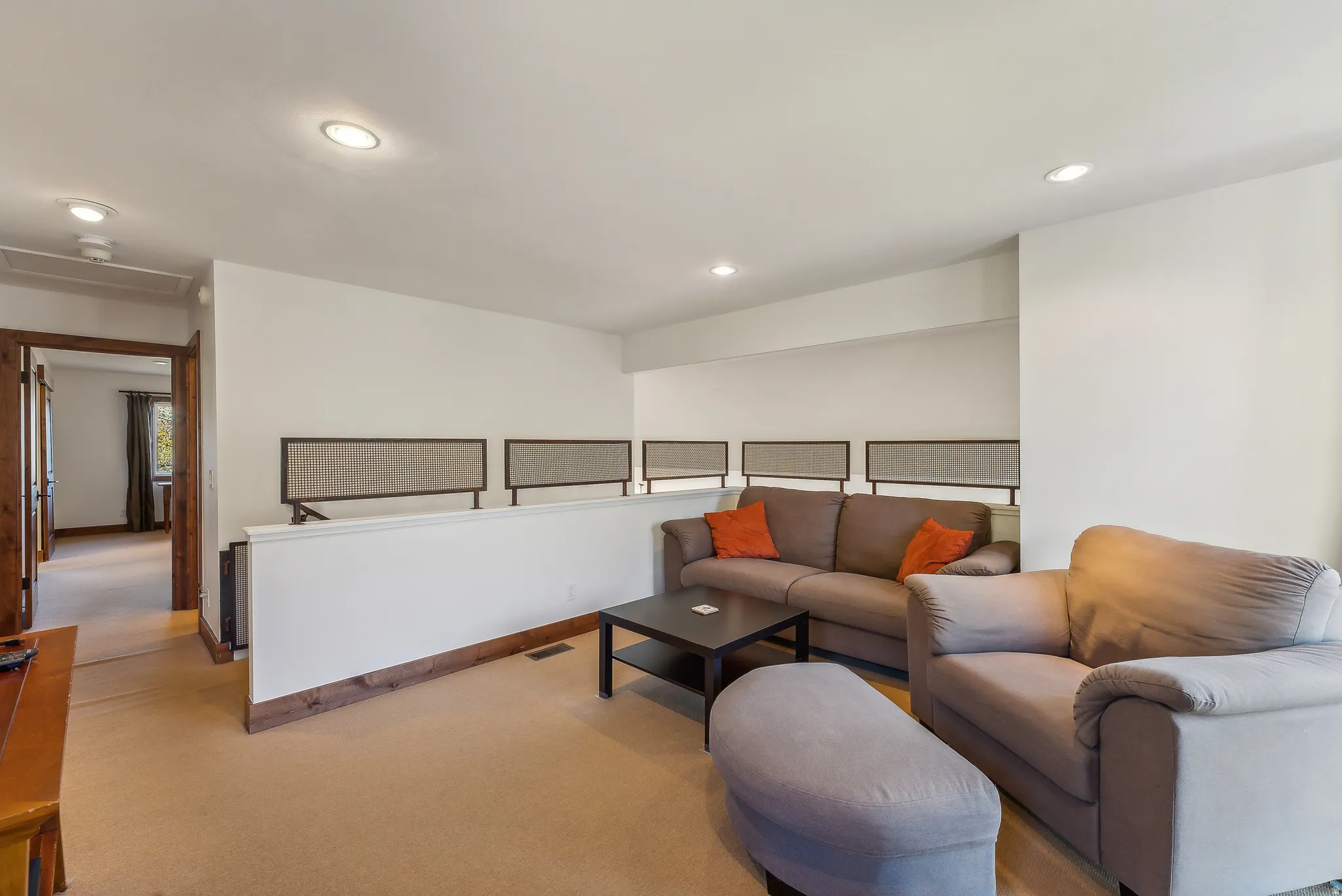 Carpeted living area featuring recessed ceiling lights, white walls, and a low partial wall with decorative panels