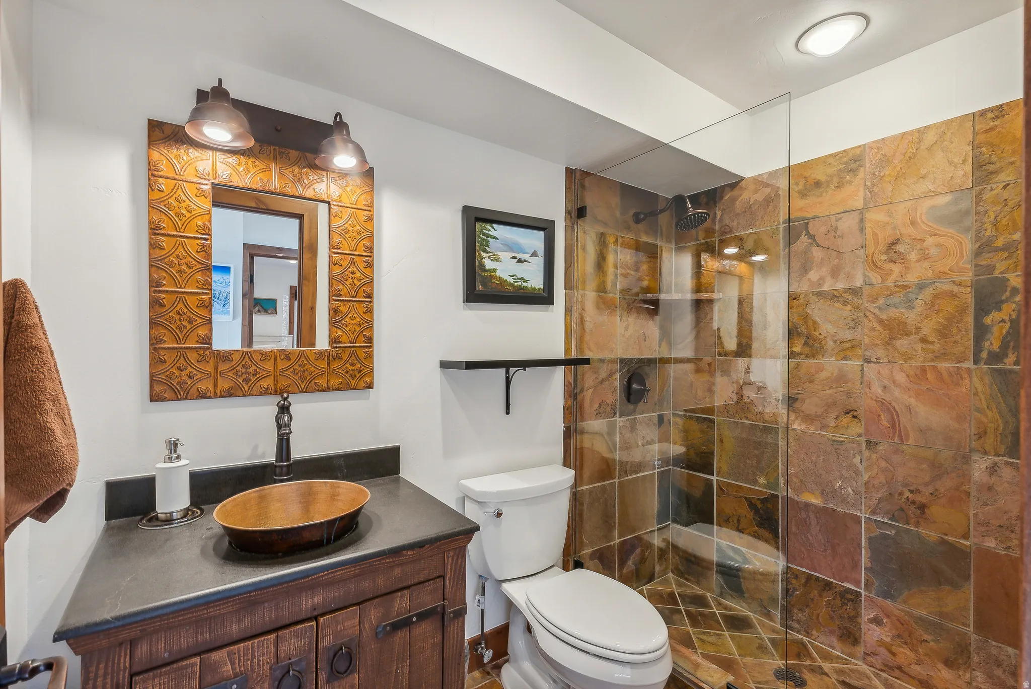 Bathroom featuring a glass-enclosed shower with full-height tile, a distressed wood vanity with a vessel sink, a coordinating framed mirror, and a wall-mounted light fixture