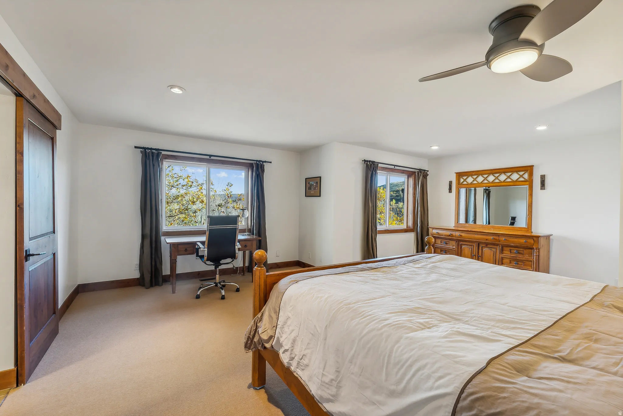 Carpeted bedroom featuring a ceiling fan with integrated lighting, recessed lighting, and a dark wood-finish door with black hardware
