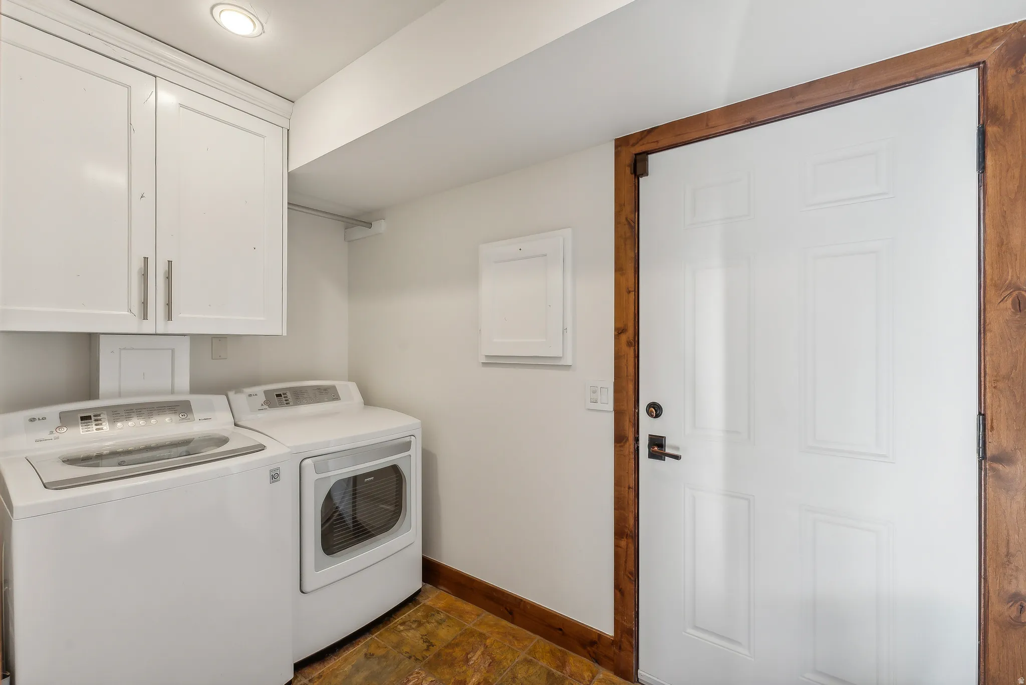 Functional utility area featuring white cabinetry, a built-in washing machine and dryer, a paneled door with wood trim, and textured flooring