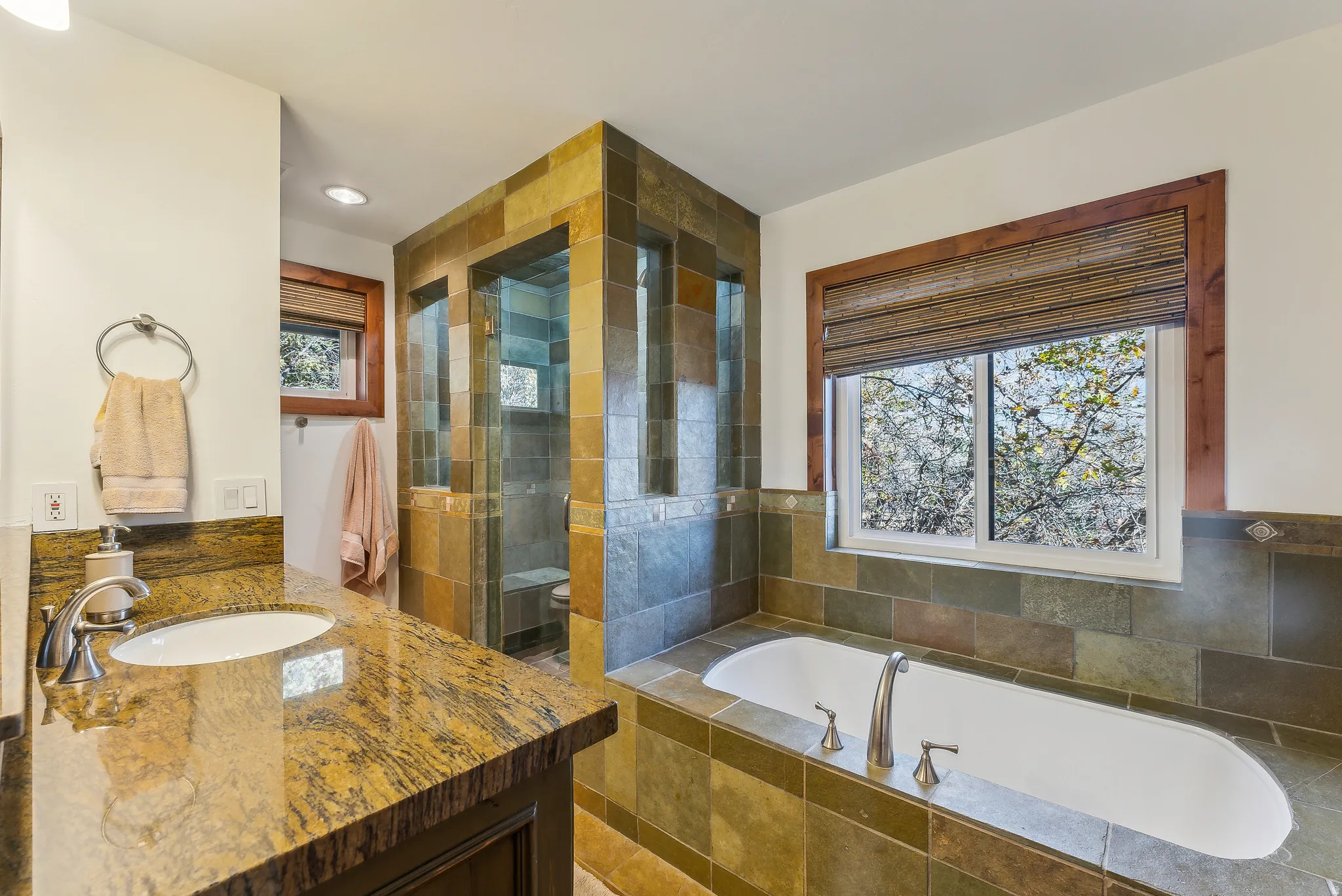 Bathroom featuring a tile-surround drop-in tub, a walk-in shower with glass enclosure, wood-framed windows, a vanity with a granite countertop, and an undermount sink