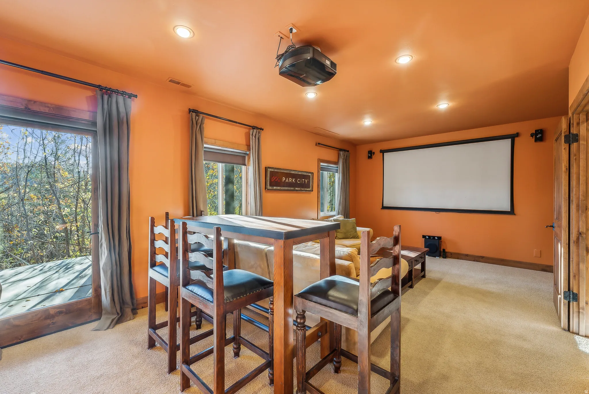 Entertainment room featuring a ceiling-mounted projector, large projection screen, recessed lighting, and direct outdoor access via a glass door
