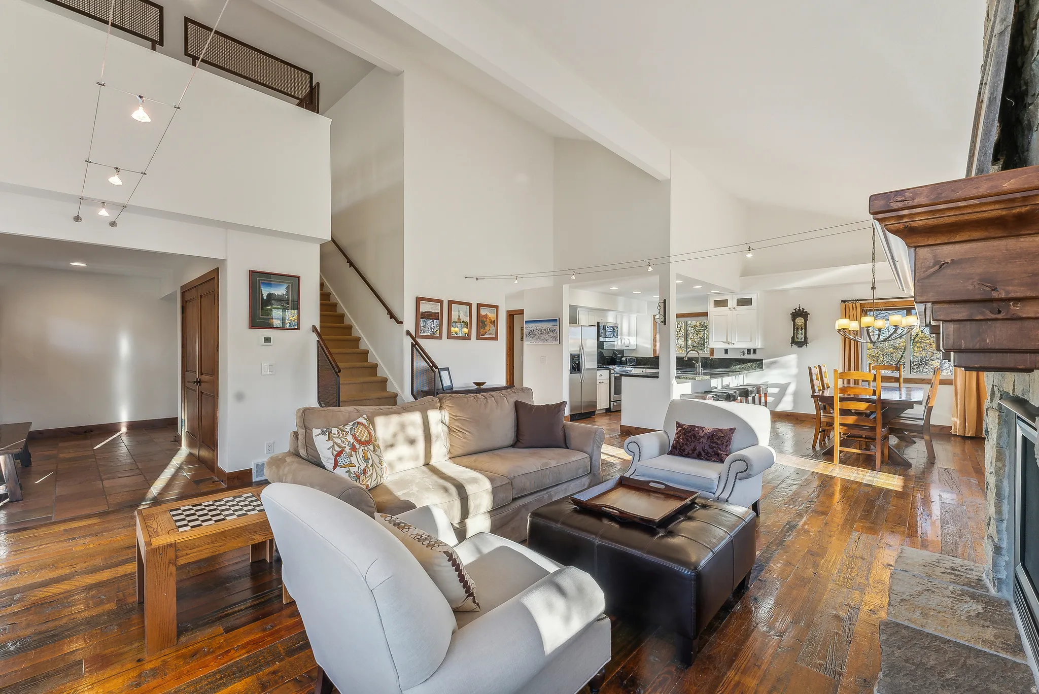 Spacious living area featuring high vaulted ceilings, rich wood-finish flooring, and a stone-clad fireplace with a substantial wood mantel