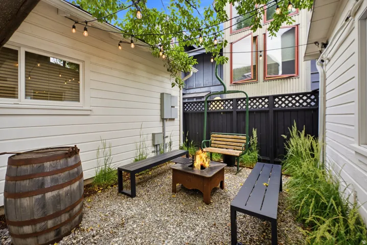 Gravel patio featuring a fire pit, string lighting, and perimeter fencing