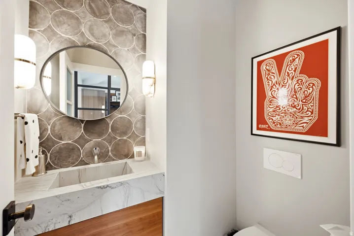Powder room featuring a circular mirror, two wall-mounted light fixtures, and a marble countertop with an integrated sink