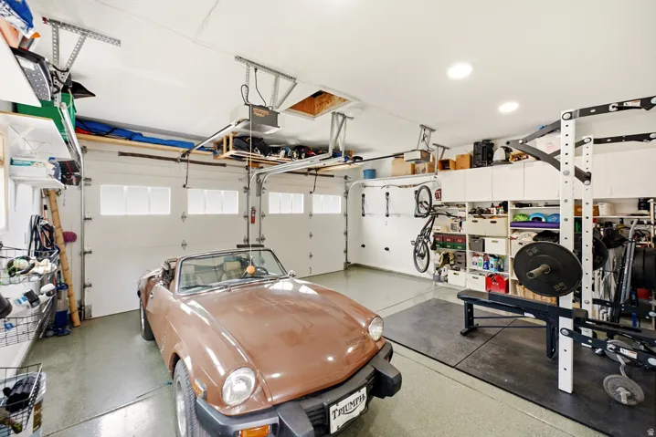 Two-car garage featuring segmented overhead doors with frosted glass panels, built-in cabinetry, overhead storage racks, recessed lighting, and epoxy flooring