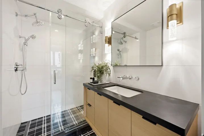 Modern bathroom featuring a wood-finish vanity with an integrated sink, dark countertop, and wall-mounted faucet