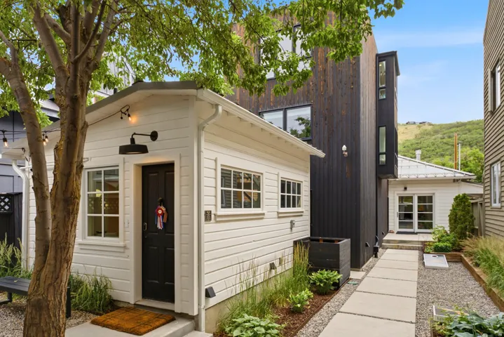 White siding structure featuring a black entry door, grid-pattern windows, and a black wall-mounted light fixture