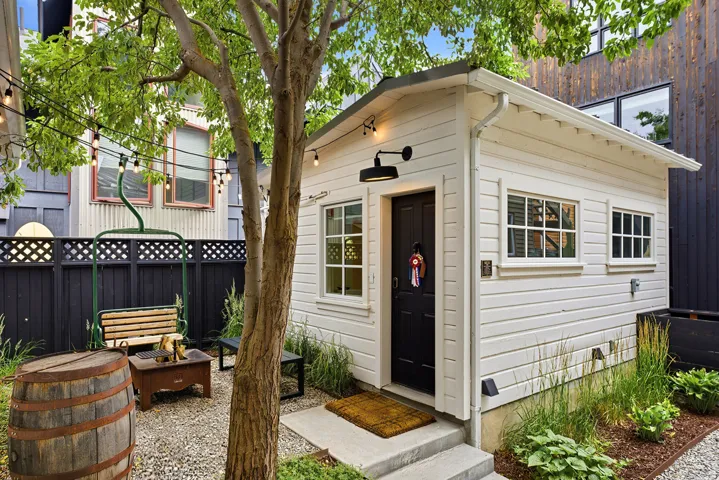 Detached accessory building featuring white horizontal siding, a black entry door, and multiple windows with white grilles