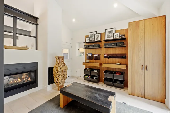 Living area with a contemporary fireplace, light wood-finish flooring, recessed lighting, and a built-in wood accent wall with integrated shelving and storage