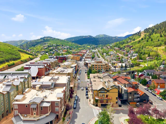 Mountain town setting featuring commercial and residential structures, extensive green hillsides, and a prominent main thoroughfare