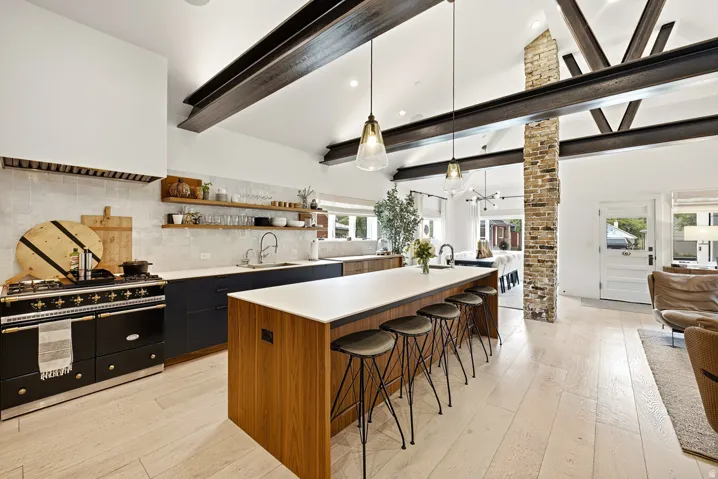 Contemporary kitchen featuring exposed beam ceiling, an oversized island with seating, a large range, white countertops, and light wood-finish flooring