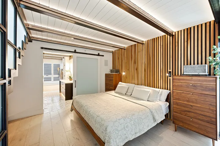 Bedroom featuring wood-finish flooring, a slatted wood-paneled accent wall, and a frosted glass barn door