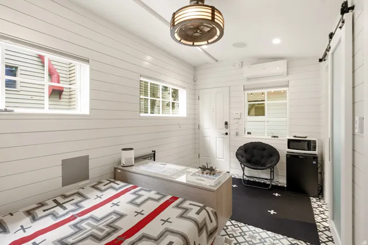 Compact living area featuring white shiplap walls, patterned floor tiles, a built-in mini-split HVAC system, a barn door, and a decorative ceiling light fixture