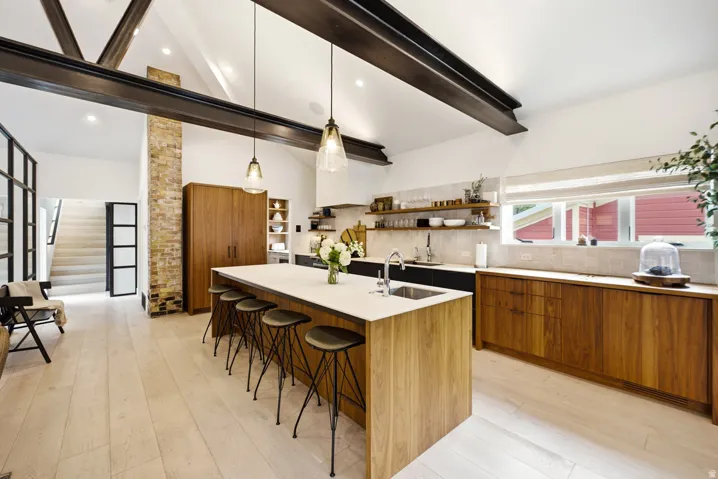 Kitchen featuring a central island with countertop seating, light wood-finish flooring, exposed ceiling beams, a brick accent column, and wood-finish cabinetry