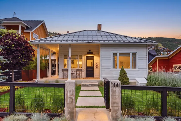 Contemporary bungalow featuring white siding, a covered front porch, and a metal roof