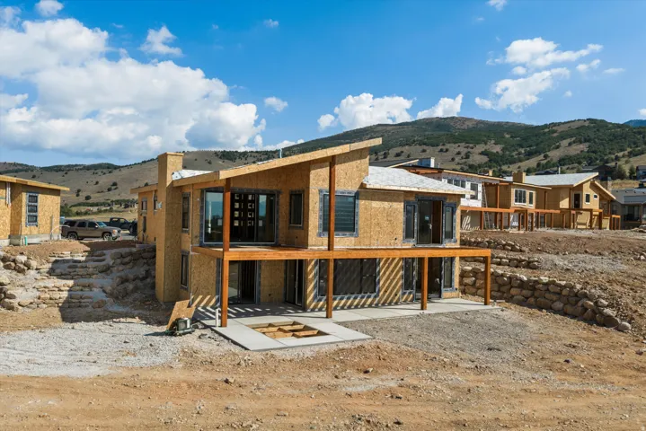 Modern architectural design featuring extensive window placement, a covered deck, and a lower-level patio