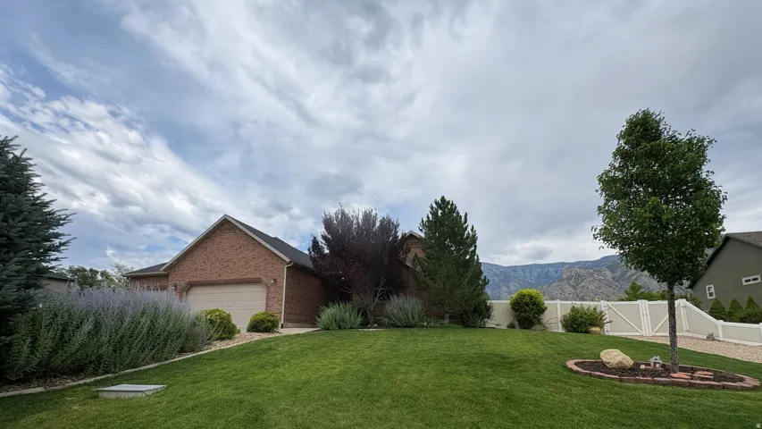 Brick exterior with an attached garage, featuring a verdant lawn, established landscaping, and a white privacy fence