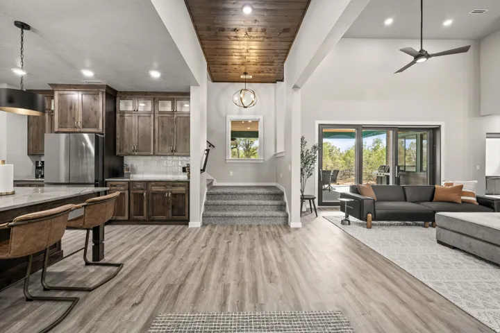 Spacious interior featuring wood-finish flooring, a contemporary kitchen with stainless steel appliances, a living area with high ceilings and a ceiling fan, a staircase with carpeted treads, and a sliding glass door opening to outdoor space