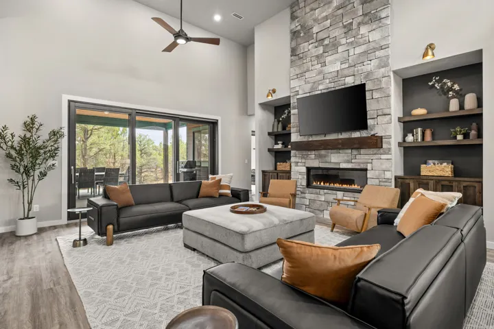 Spacious living area featuring a vaulted ceiling with a ceiling fan, a stone-clad fireplace with an integrated linear firebox, and built-in shelving