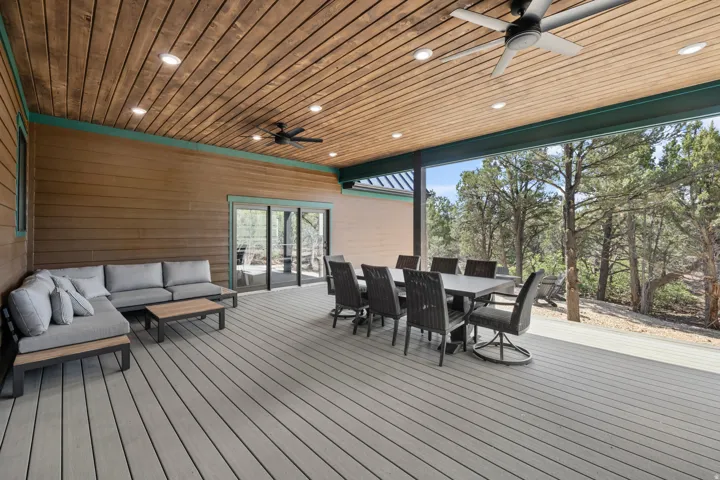 Expansive covered deck featuring composite decking, wood-plank ceiling with recessed lighting and ceiling fans, and a panoramic tree-lined backdrop