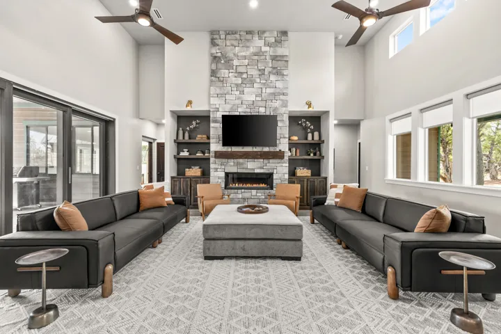 Vaulted living area featuring a floor-to-ceiling stone fireplace with a wood-beam mantle, built-in shelving, and dual ceiling fans
