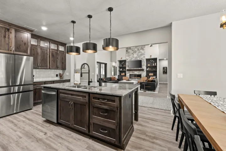 Gourmet kitchen featuring a large central island with sink, wood-finish cabinetry, stainless steel appliances, and sleek pendant lighting