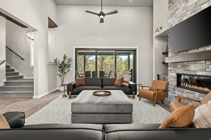 Spacious living area featuring a vaulted ceiling with a ceiling fan, a linear fireplace set in a stacked stone surround, and lvp flooring