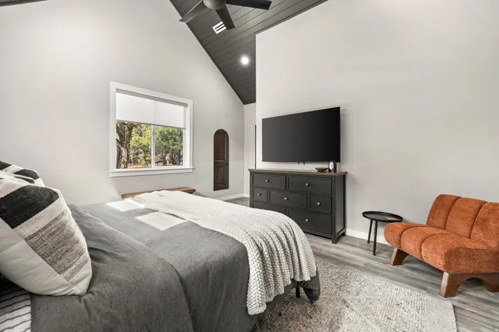 Vaulted ceiling with dark wood paneling, light gray walls, window with roller shade, wood-finish flooring