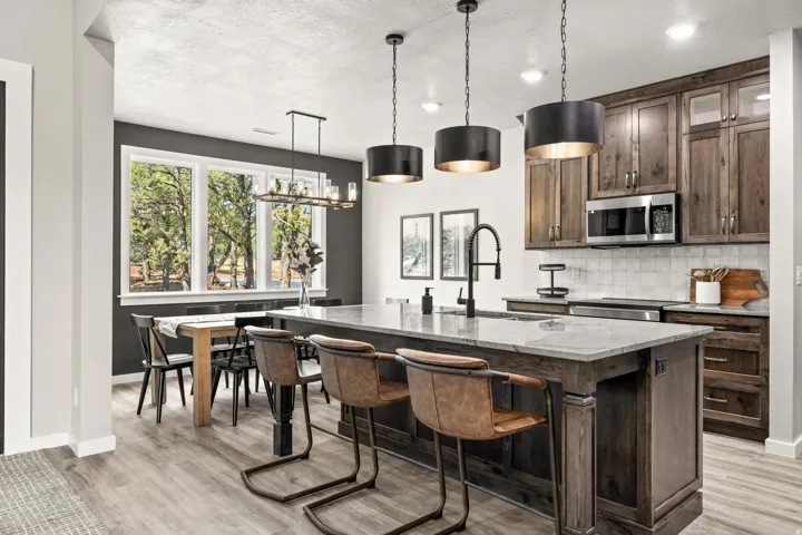 Open-concept kitchen featuring wood-finish flooring, a large island with seating, dark wood cabinetry, stainless steel appliances, and a tiled backsplash