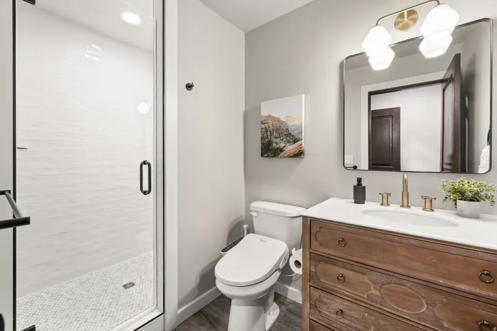 Bathroom featuring a glass-enclosed shower with subway tile surround and hexagonal mosaic floor, a vanity with a white countertop and gold-toned faucet, and wood-finish flooring