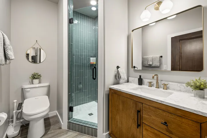 Contemporary bathroom featuring a glass-enclosed shower with vertical blue-green tile, a wood-finish vanity with a white countertop, a rectangular undermount sink, and brass fixtures