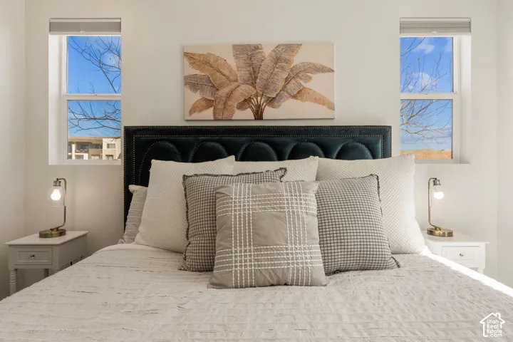 Bedroom featuring a dark upholstered headboard, white walls, and two single-pane windows with white trim