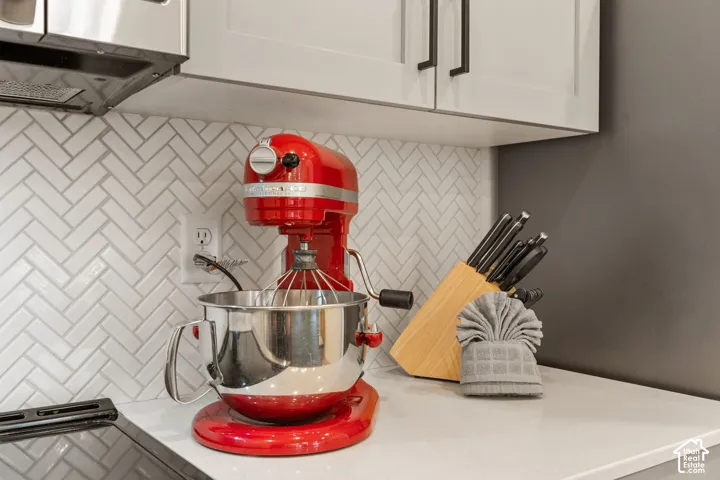 Kitchen detail featuring a herringbone tile backsplash, white shaker-style cabinetry with matte black hardware, and a solid surface countertop