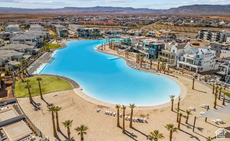 Expansive community lagoon featuring clear blue water, surrounding sandy beaches, mature palm trees, and modern residential architecture