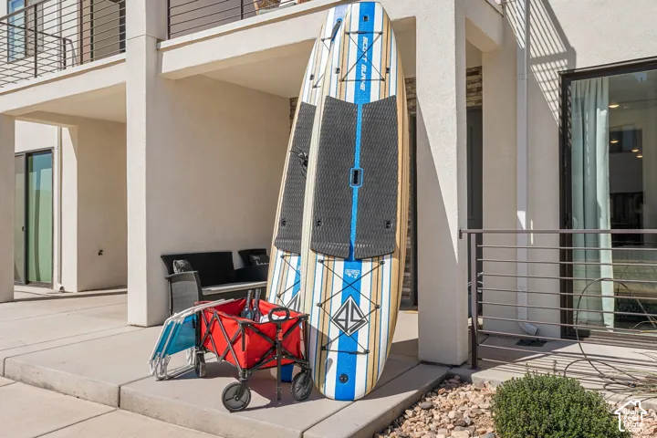 Contemporary exterior with smooth stucco finish, large glass sliding doors, a second-story balcony with horizontal metal railings, a covered patio space, and a concrete paver walkway