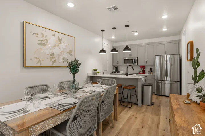 Open-concept kitchen and dining area featuring light wood-finish flooring, a kitchen island with seating, pendant lighting, and stainless steel appliances