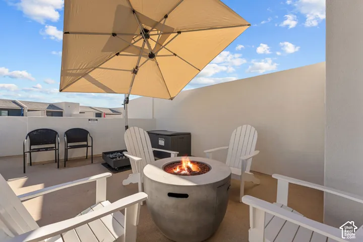 Rooftop patio featuring a concrete fire pit, sun umbrella, and white Adirondack chairs