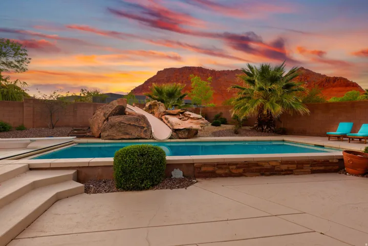 Outdoor swimming pool featuring a rock-slide, surrounding patio, and stacked stone pool surround