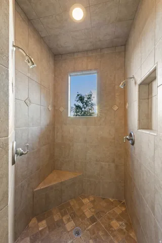 Tiled shower with a corner bench, recessed niche, two shower heads, and a window