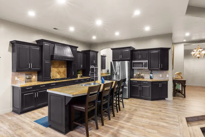 Gourmet kitchen featuring dark cabinetry, lighter countertops, a central island with seating, stainless steel appliances, and wood-finish flooring