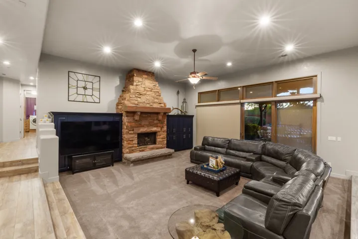 Spacious living area featuring a stacked stone fireplace with a substantial wood mantel, recessed lighting, and a ceiling fan