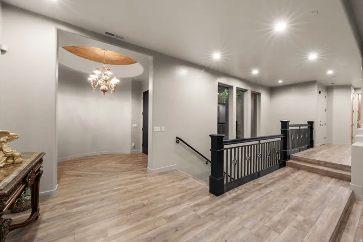 Curved entryway featuring a chandelier with a wood-finish recessed ceiling, wood-finish flooring, recessed lighting, and a dark metal railing
