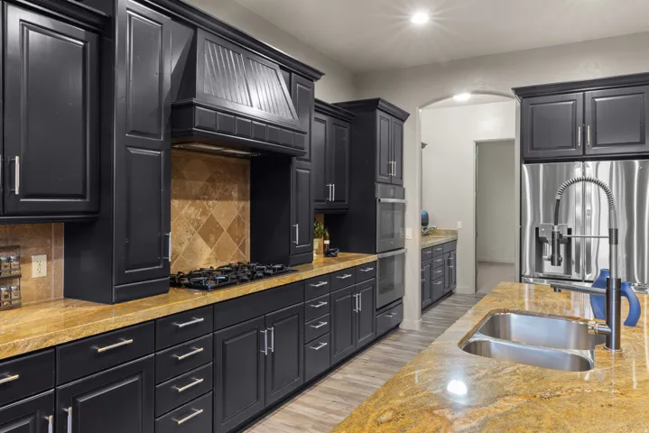 Kitchen featuring dark cabinetry, natural stone countertops, stainless steel appliances, a gas cooktop, and an undermount double-basin sink with a flexible faucet