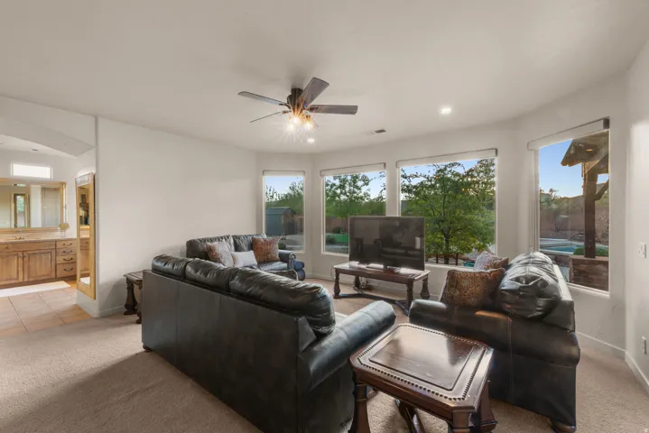Spacious interior featuring a lighted ceiling fan, carpeted flooring, and multiple large windows