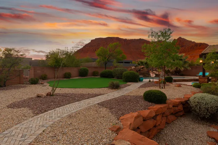 Desert landscape featuring a putting green, a swimming pool, and a paver pathway
