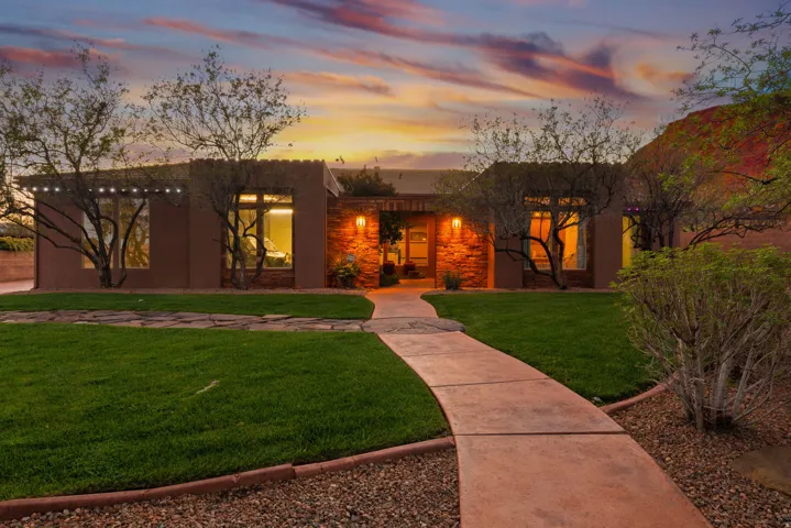 Stucco exterior residence with stone accent walls, a curved concrete pathway, and mature trees framing the entrance